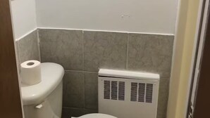 Une petite salle de bain propre, avec des toilettes, un radiateur et un rouleau de papier toilette accroché au mur.