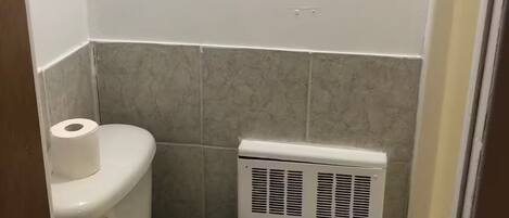 A small, clean bathroom with a toilet, a radiator, and a roll of toilet paper on the wall.