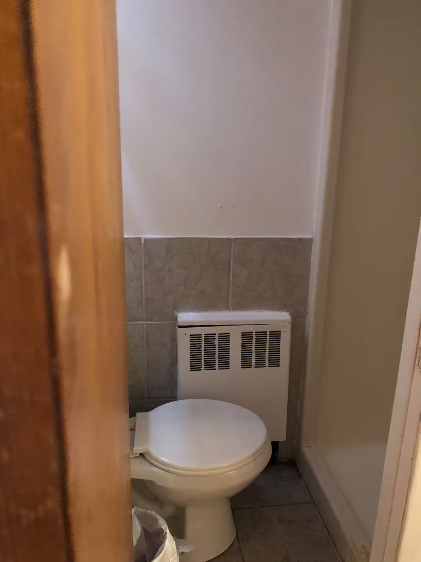 A small, narrow bathroom with a white toilet and a wall-mounted heater.