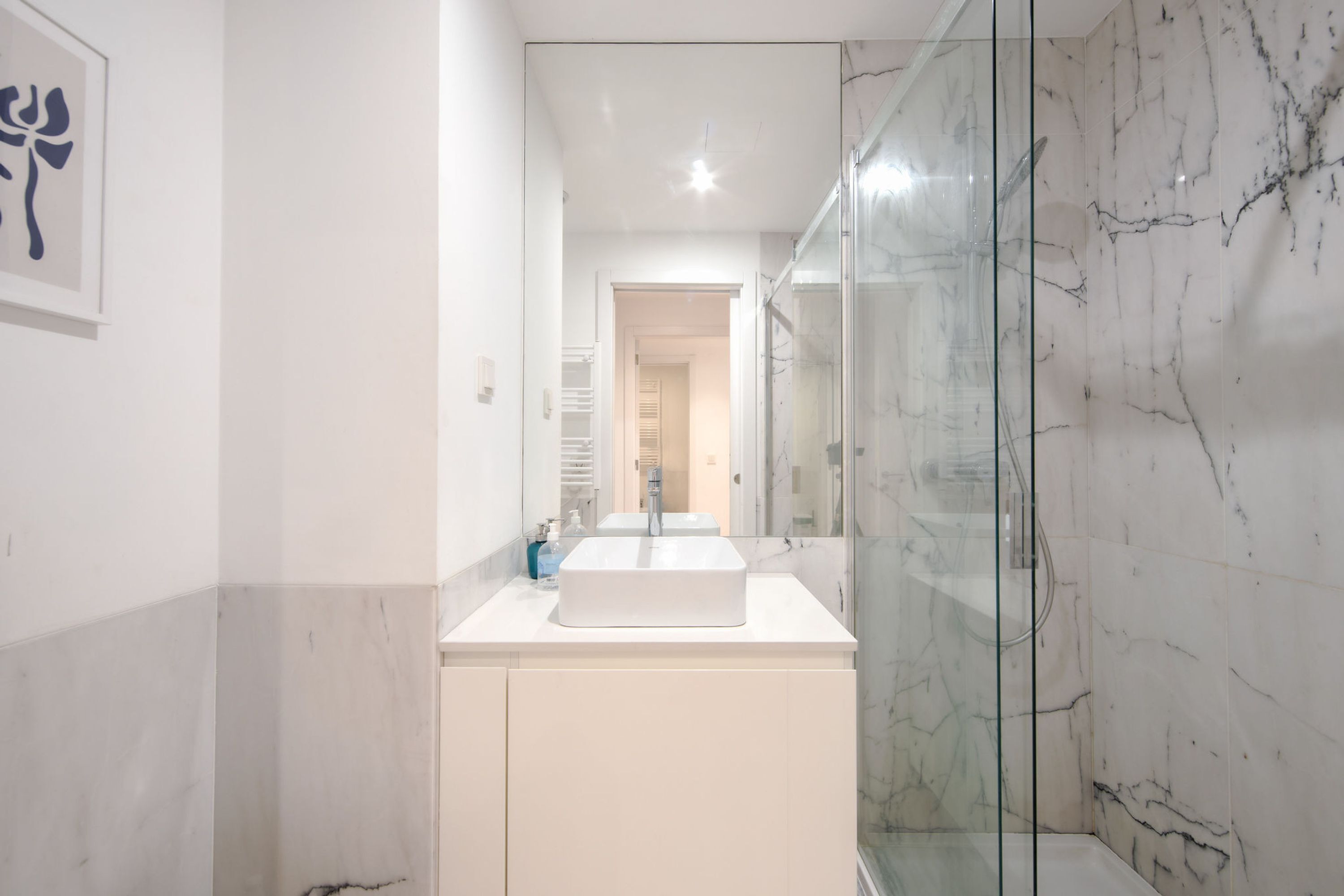 Un baño moderno con cabina de ducha de vidrio, un lavamanos blanco y una obra de arte enmarcada en la pared.