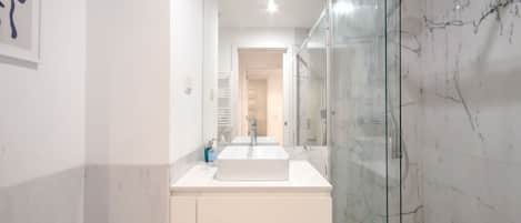 Un baño moderno con cabina de ducha de vidrio, un lavamanos blanco y una obra de arte enmarcada en la pared.