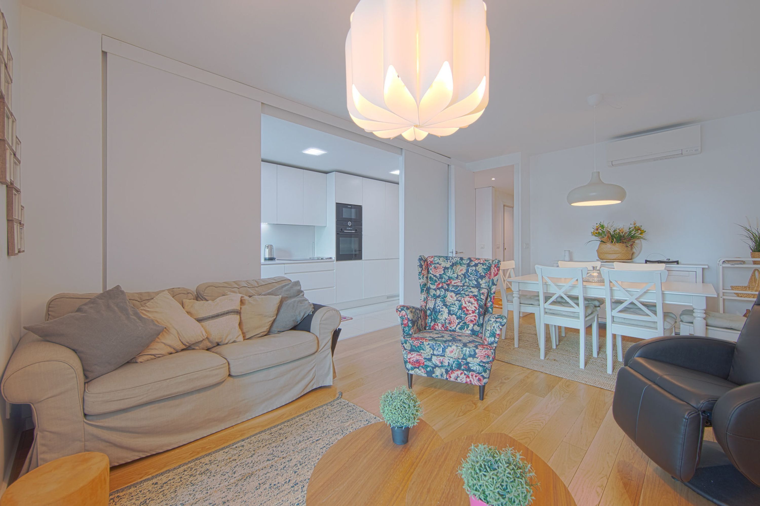 A modern living room with a sofa, a floral armchair, and a dining area with a table and chairs.