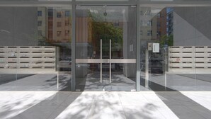 Ein moderner Gebäudeeingang mit Glastüren, einem Metallgitter und einem gefliesten Boden.