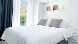 A modern bedroom with a large bed, white walls, and a view of the city through a window. - Central and Fully-Equipped (Kavala)