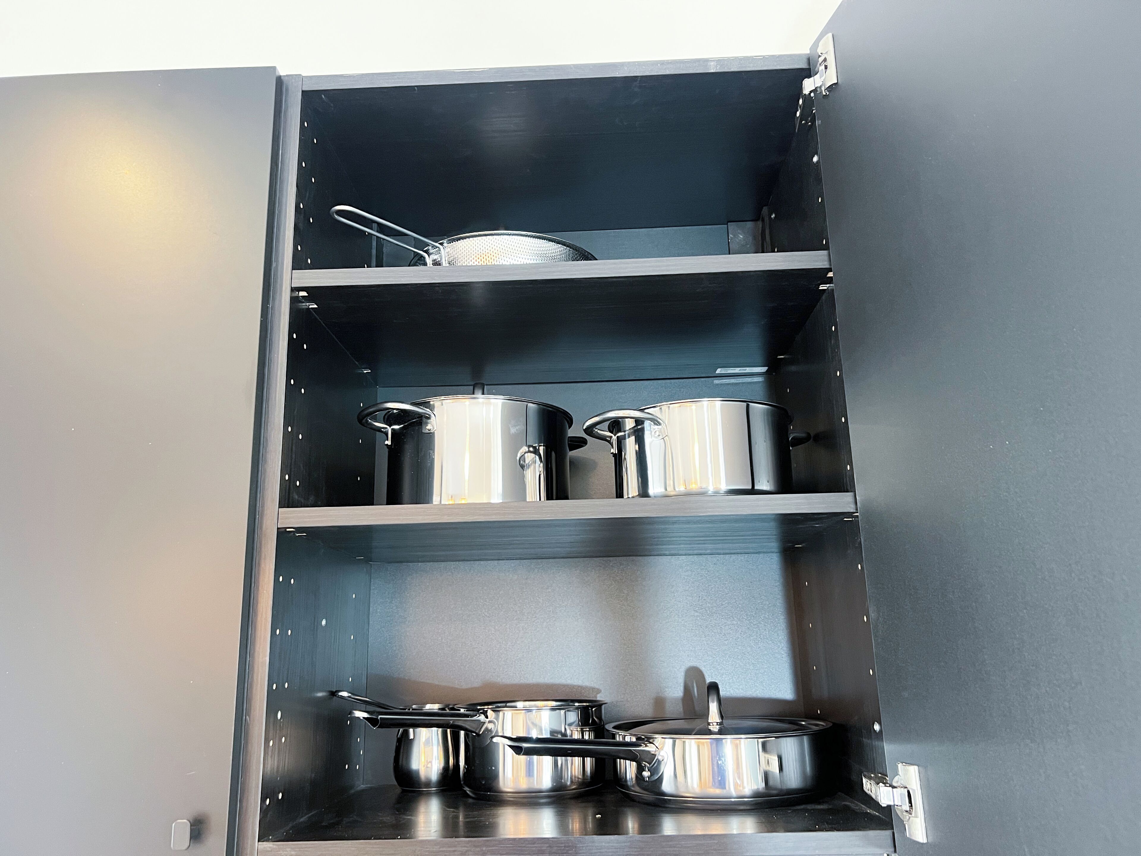 A kitchen cabinet with stainless steel cookware, including pots and pans.