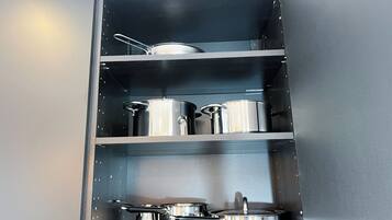 A kitchen cabinet with stainless steel cookware, including pots and pans.