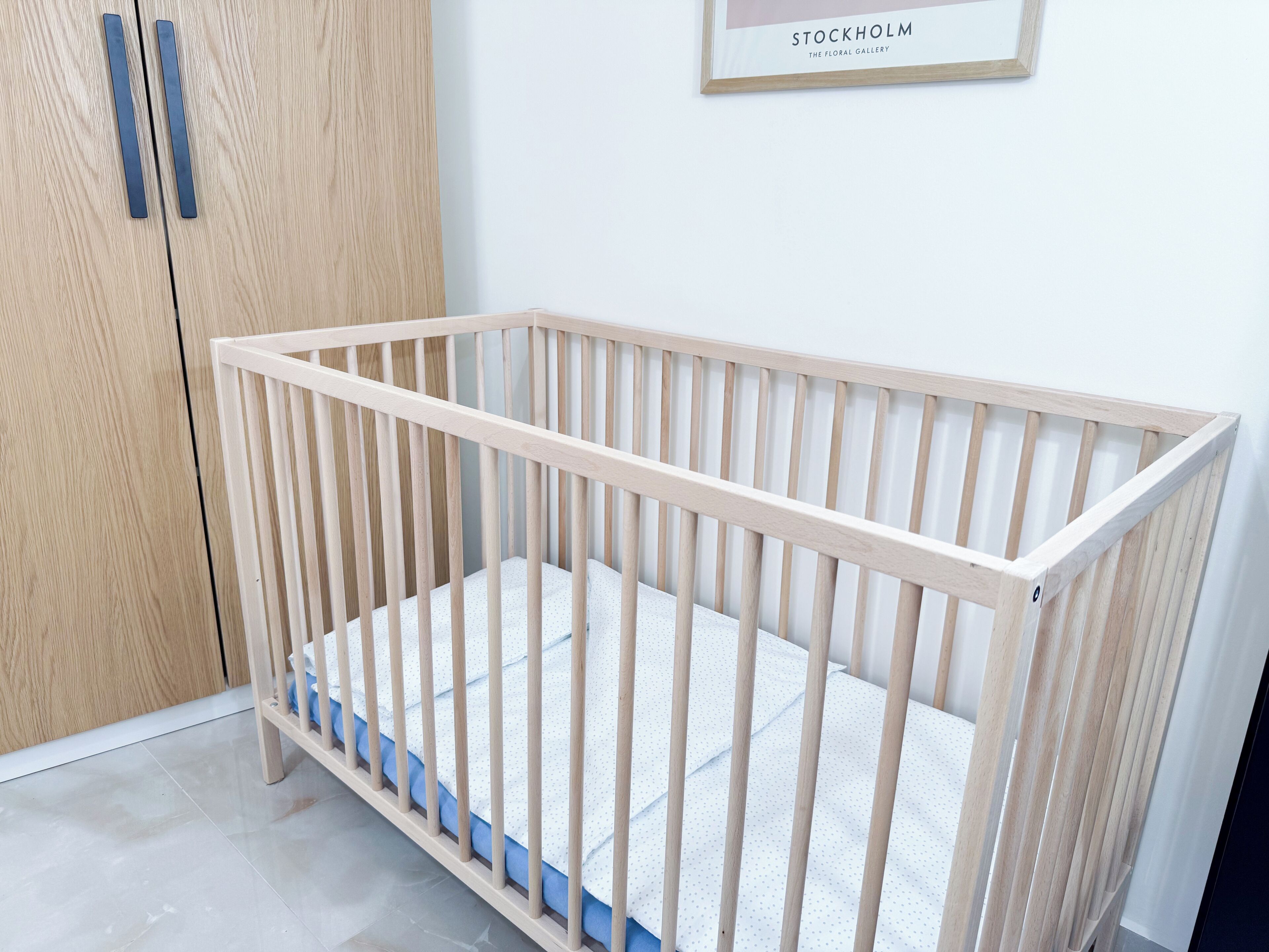 Een houten wieg met een wit matras in een kamer met een houten garderobe en een lijst met een foto erop.