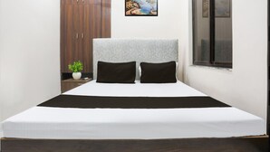 A bedroom with a bed, a nightstand with a plant, a wardrobe, and a window with a view. - Hotel S Grand  (Prayagraj)