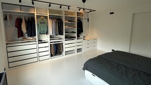 Une chambre à coucher comprenant un lit, un dressing avec de nombreux tiroirs et étagères, ainsi qu’une tringle pour suspendre les vêtements.