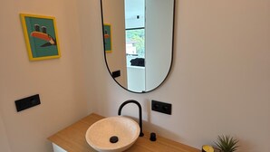 Une salle de bain avec un lavabo rond, un miroir, une petite plante et un tableau au mur.