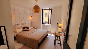 A bedroom with a bed, bedside table, lamp, and a view of the outside. - In the heart of the Old Town with a breathtaking view! (Annecy)