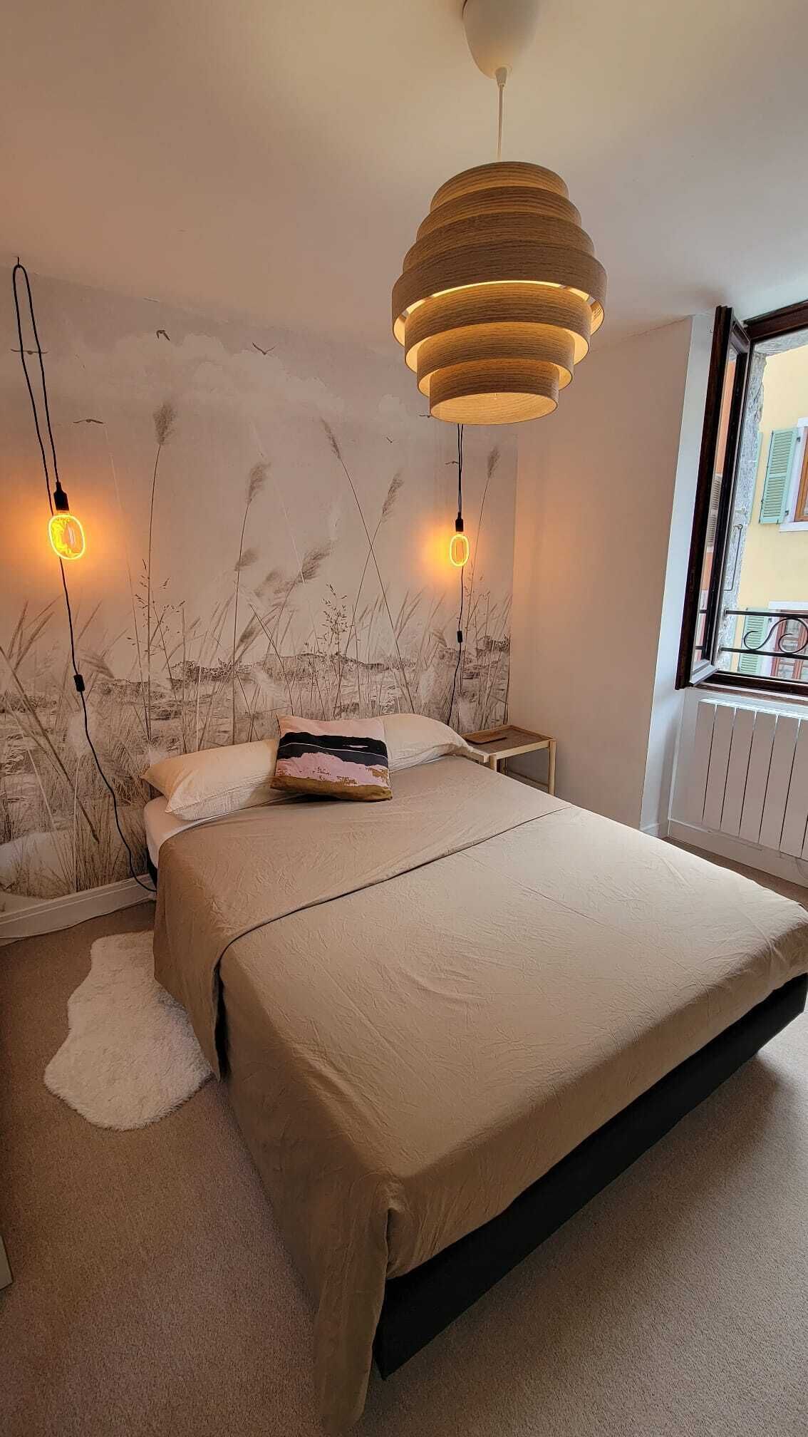 A bedroom with a large bed, a wooden headboard, two bedside lamps, and a view of the outside through a window.
