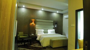 A hotel room with a large bed, a nightstand, a chair, and a small table. - Nomsy Luxury Service Apartments  (Owerri)