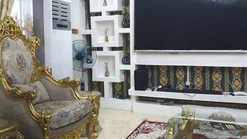 A living room with a large flat-screen TV, ornate golden furniture, and patterned wall decorations.