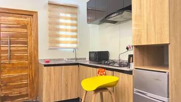 A kitchen with wooden cabinets, a black microwave, a yellow stool, and a stainless steel refrigerator.