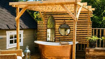 A wooden pergola with a hot tub, wicker furniture, and a house in the background.