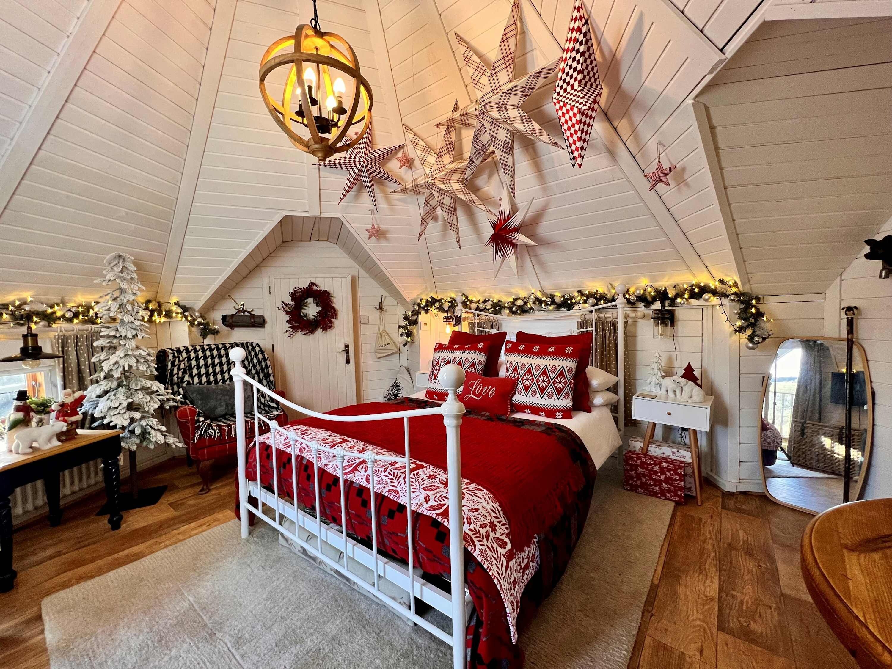 A cozy bedroom with a sloped ceiling, a bed with red bedding, a white dresser, and Christmas decorations.