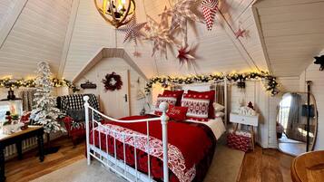 A cozy bedroom with a sloped ceiling, a bed with red bedding, a white dresser, and Christmas decorations.