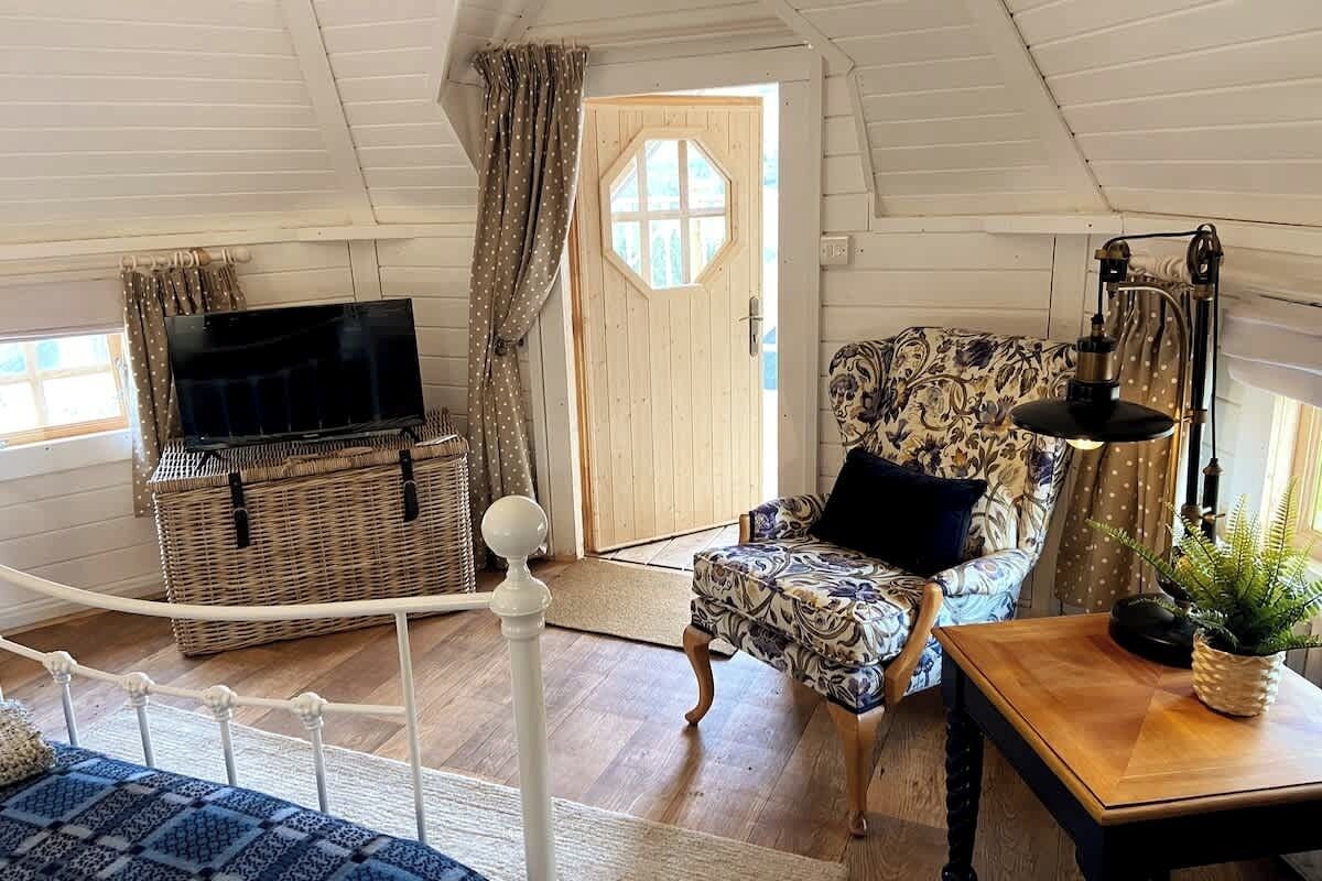 Une pièce chaleureuse, dotée d’un téléviseur, d’un fauteuil à motifs, d’une table en bois et d’un panier en osier.
