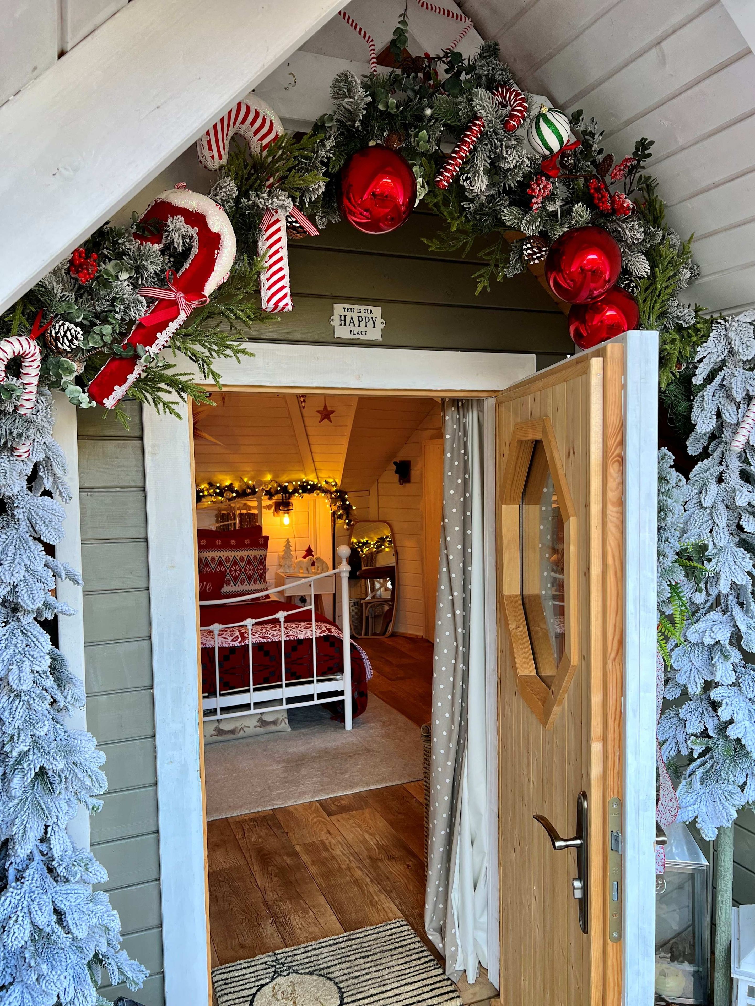 Una habitación acogedora con una cama, una puerta de madera y adornos festivos, incluyendo un cartel que dice 'THIS IS OUR HAPPY PLACE'.