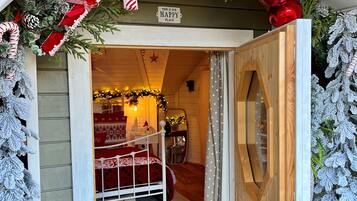Una habitación acogedora con una cama, una puerta de madera y adornos festivos, incluyendo un cartel que dice 'THIS IS OUR HAPPY PLACE'.
