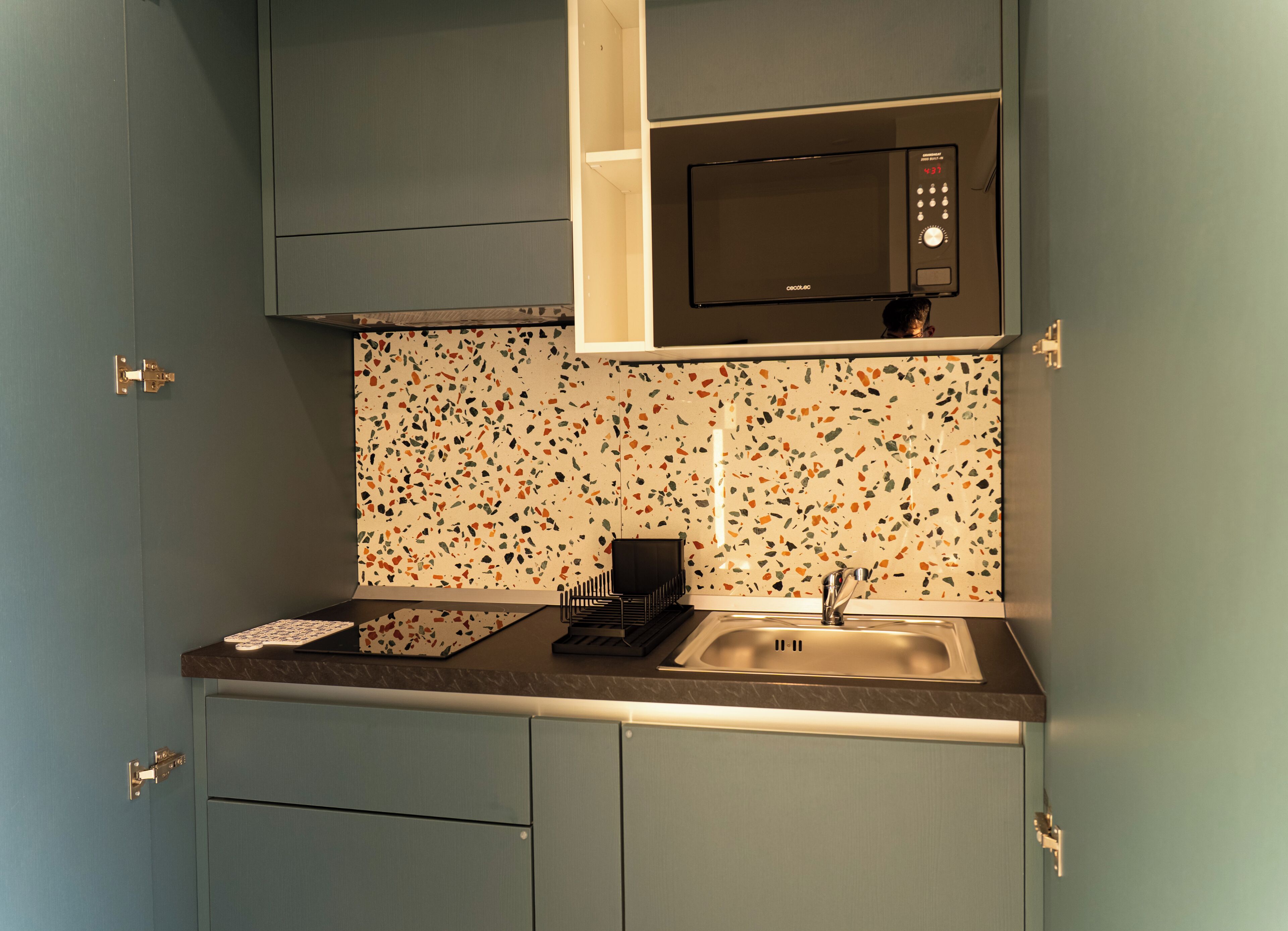 Una cocina con microondas, pileta y salpicadero con un diseño de mosaico granulado.