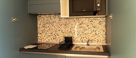 Una cocina con microondas, pileta y salpicadero con un diseño de mosaico granulado.