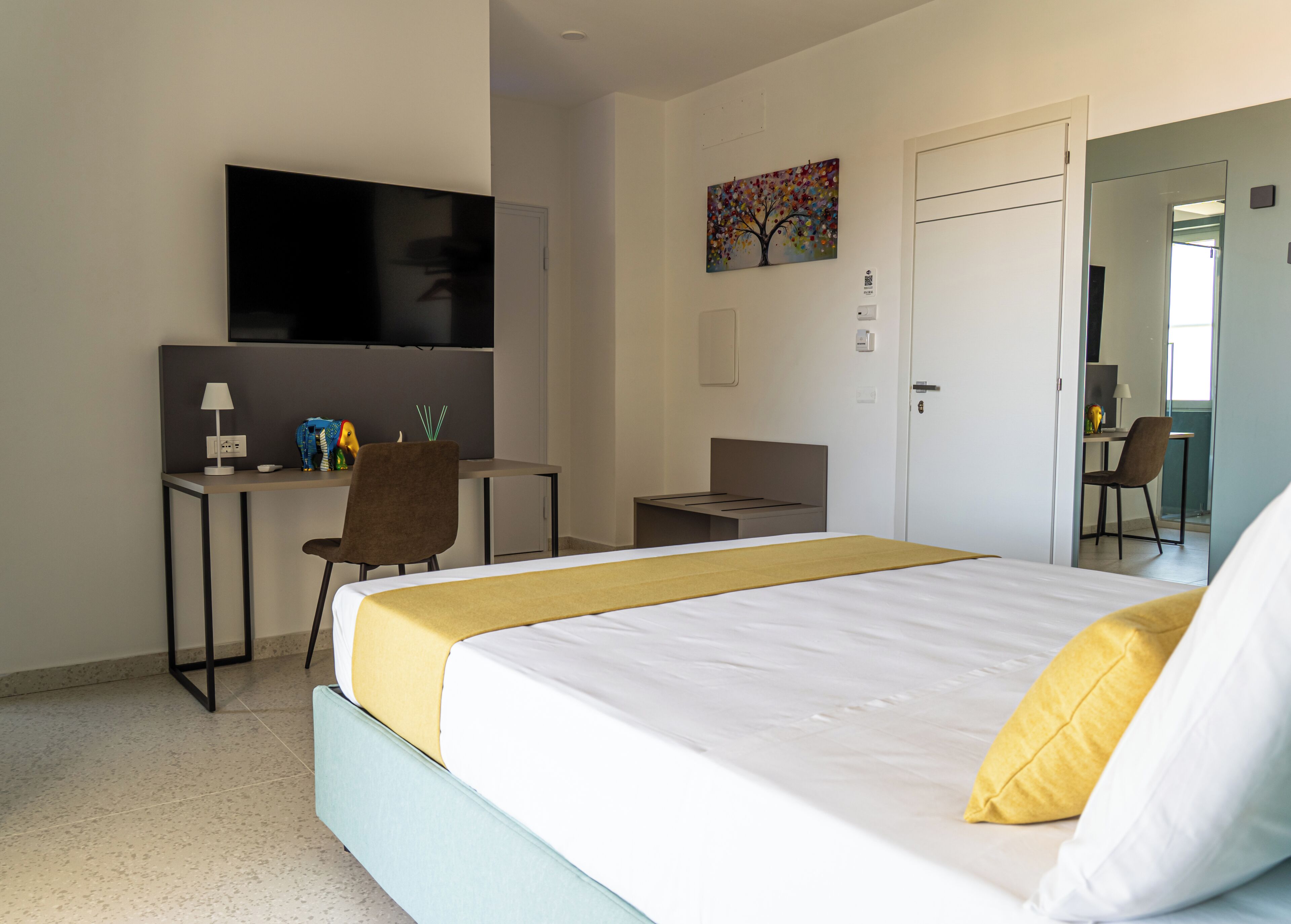 A hotel room with a bed, a desk, a chair, a TV, and a door.