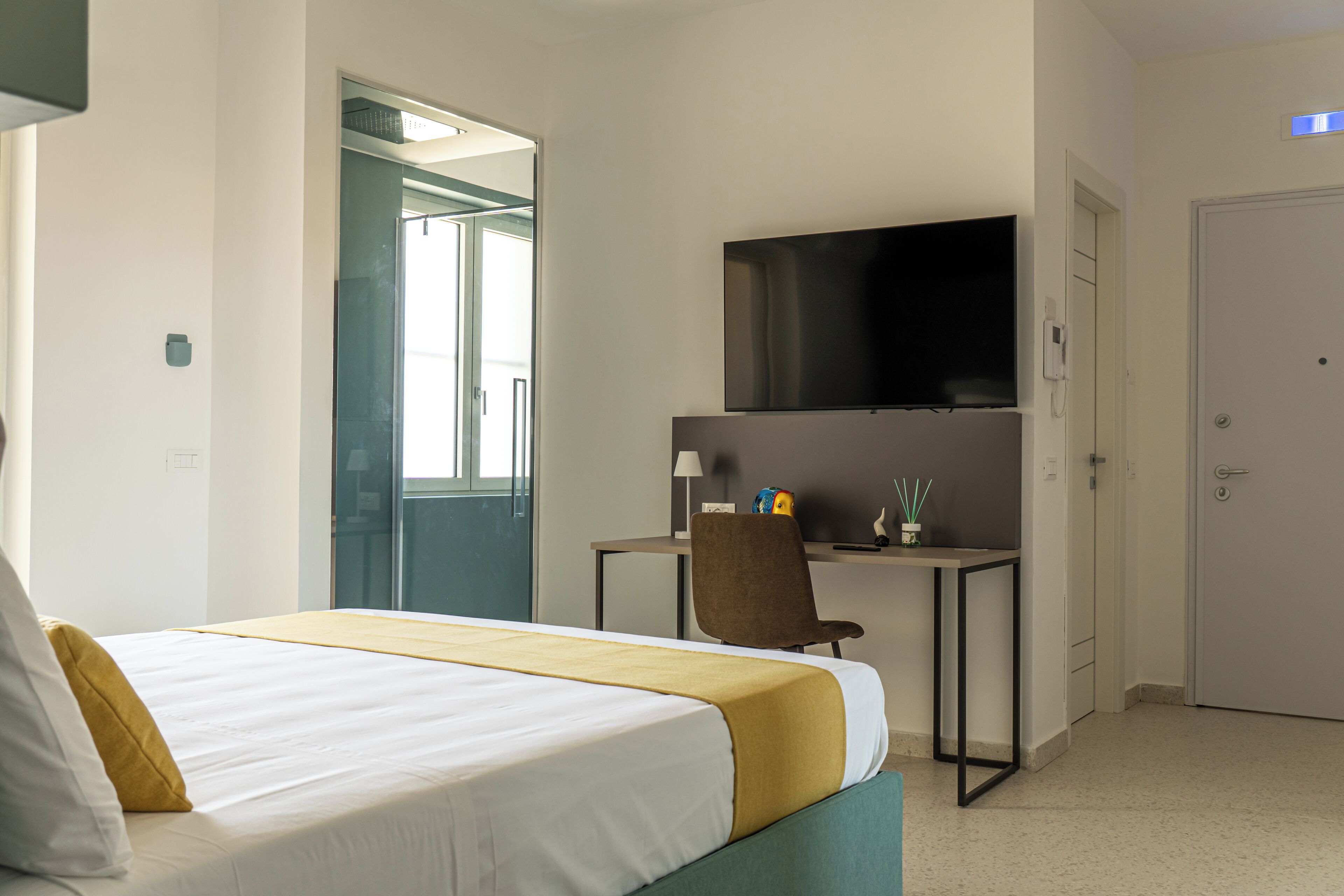 Una habitación de hotel con cama, escritorio, silla, televisor y puerta.