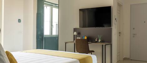 Una habitación de hotel con cama, escritorio, silla, televisor y puerta.