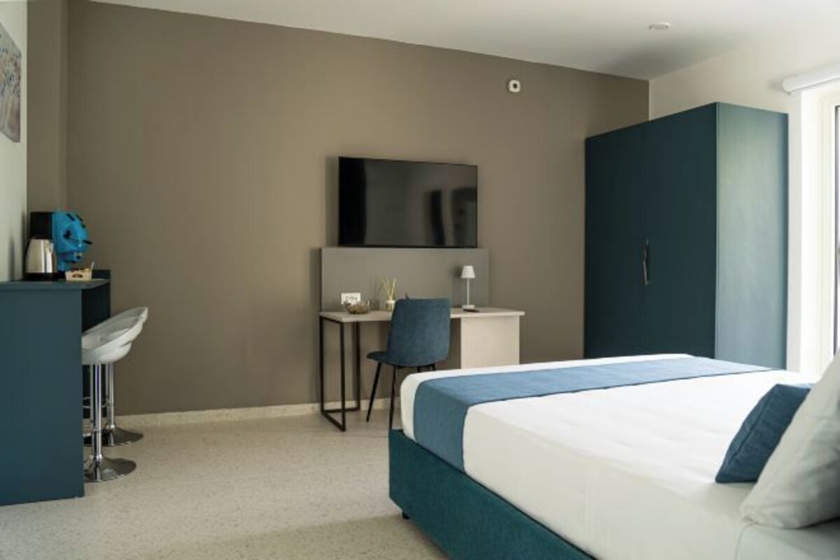 Una habitación de hotel con cama, escritorio, silla, televisor y armario.