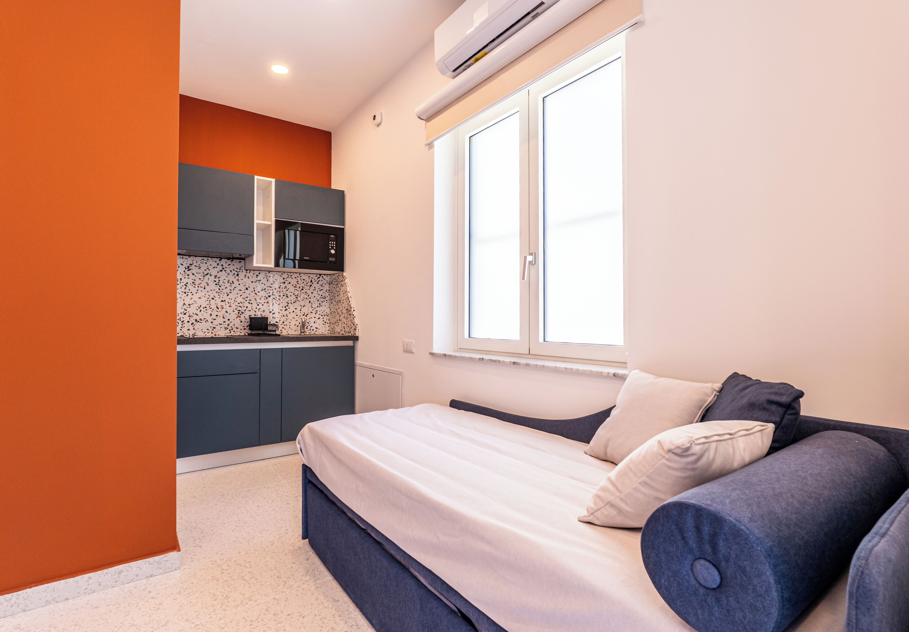 Habitación pequeña con cama, kitchenette y ventana.