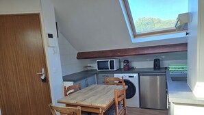 Cocina compacta con mesa y sillas de madera, lavadora, microondas y cafetera.