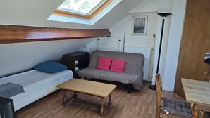 Una habitación con cama doble superior, un sofá con cojines rojos, una mesita, una silla y un radiador.