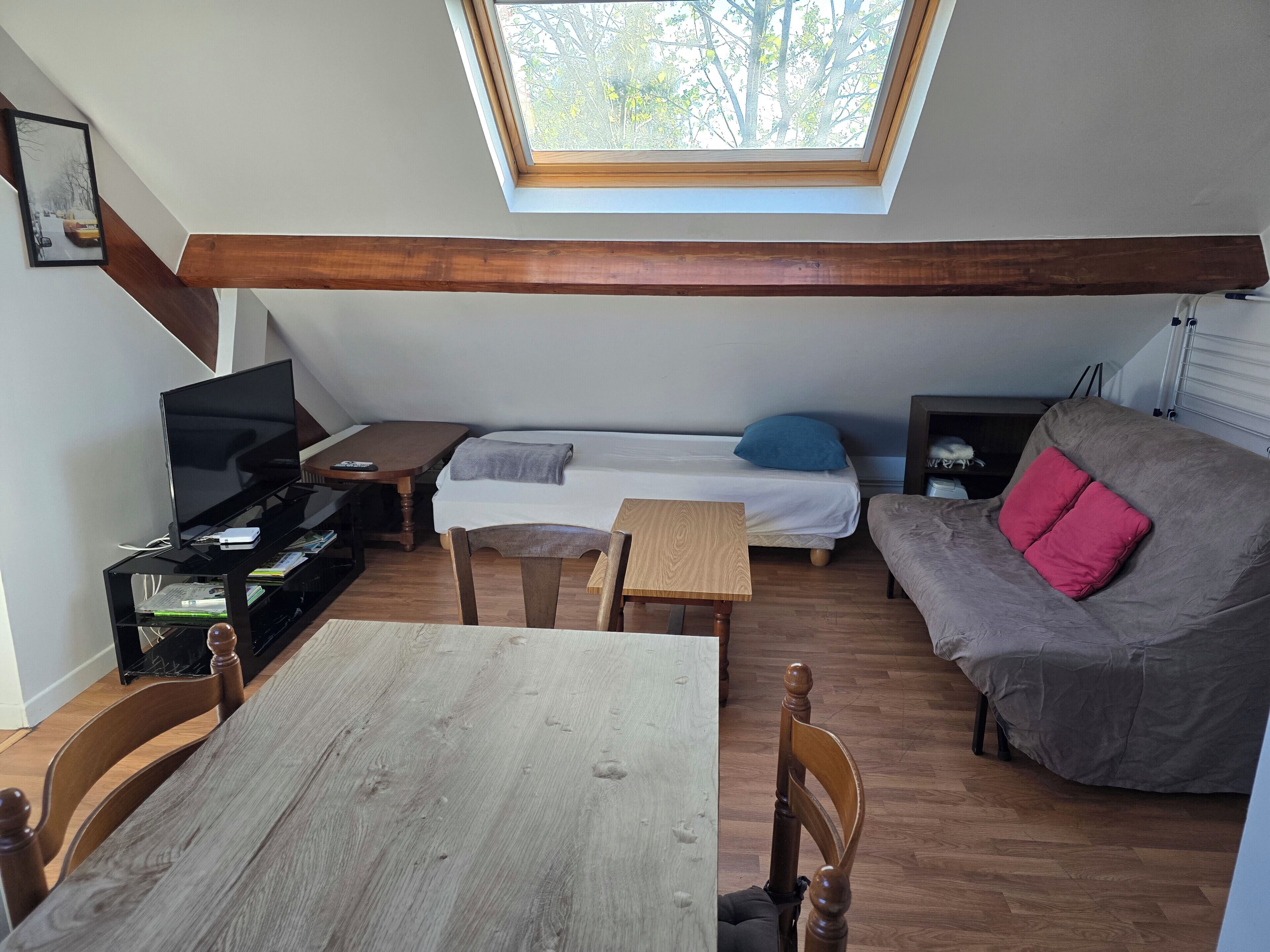 Ein Loft-Zimmer mit Dachfenster, einem Bett, einer Couch, einem Fernseher und einem Esstisch.