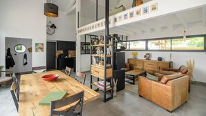 Een ruime woonkamer met een houten eettafel, leren bank en een boekenkast.