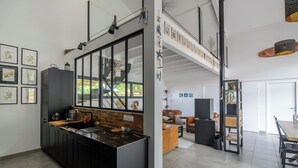 Een moderne keuken met een groot eiland, een eetgedeelte met een houten tafel, en een open zolderruimte met een trap.