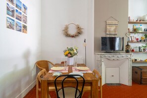 Ein Essbereich mit einem Holztisch, gedeckt für zwei Personen, einer Blumenvase und einem Fernseher auf einem weißen Schrank.