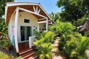A wooden house with a porch, surrounded by lush greenery and palm trees.