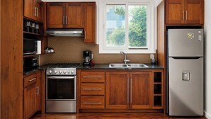 Una cocina con gabinetes de madera, un refrigerador de acero inoxidable, una estufa y una ventana con vista a la vegetación.