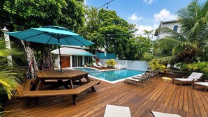 Una terraza de madera con piscina, sillas de descanso y una mesa con sombrilla.
