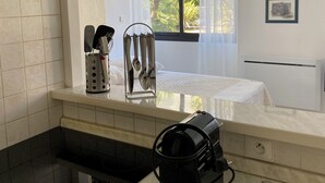 A modern kitchen with a built-in stove, a coffee maker, and a window with a view of palm trees. - Studio 26 m2 with pool & private parking (Juan-les-Pins)