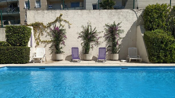 A swimming pool with clear blue water, surrounded by potted plants and white lounge chairs. - Studio 26 m2 with pool & private parking (Juan-les-Pins)
