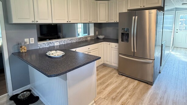 A modern kitchen with white cabinets, a stainless steel refrigerator, and a granite countertop.