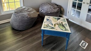 A room with a ceiling fan, two bean bags, a table with a floral design, and a door with glass panels.