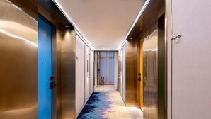 A modern hotel corridor with metallic doors, a blue door on the left, and a carpeted floor.