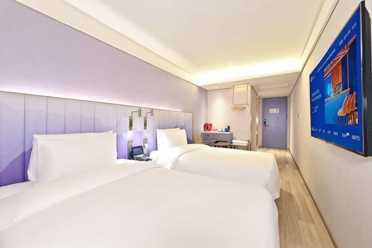 Habitación de hotel con dos camas, un escritorio, una silla, un televisor y la puerta del baño.