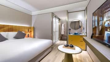 A modern hotel room with a large bed, a bedside table, a mirror, and a view of the city.