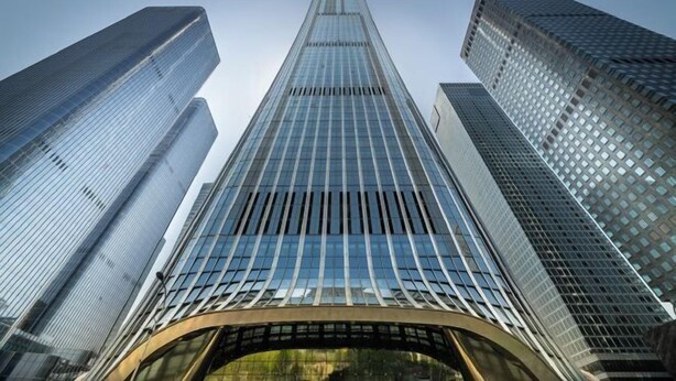 A modern skyscraper with a curved glass facade and a prominent central spire.