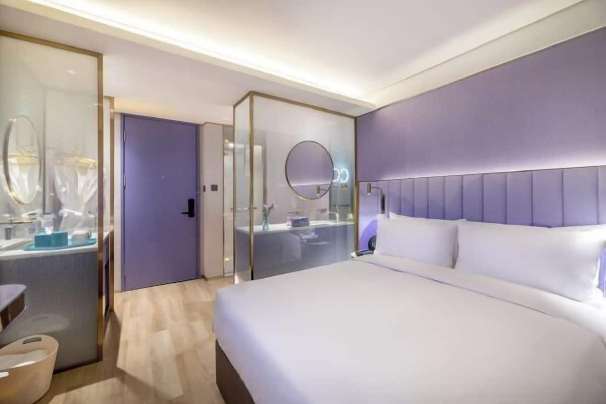 Una habitación de hotel moderna con una cama grande, un tocador con espejo y un vestidor.